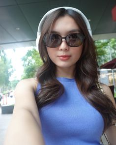 a woman wearing sunglasses and headphones taking a selfie with her hand on her hip