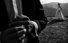 a woman in a wedding dress standing on top of a hill next to a man