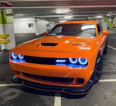 an orange sports car is parked in a parking garage with its lights on and it's hood up