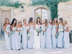 a group of women standing next to each other in front of a stone building holding bouquets