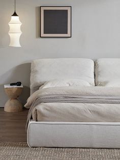 a white bed sitting on top of a wooden floor next to a wall mounted light