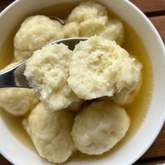 a white bowl filled with dumplings sitting on top of a wooden table next to a spoon