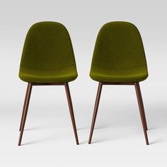 two green chairs sitting side by side in front of a white background and one with wood legs