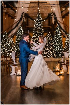 a bride and groom dancing in front of christmas trees at their wedding reception, with lights on the walls behind them