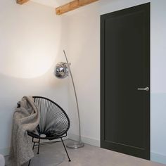 a room with a black door and a white chair in front of it, next to a metal floor lamp