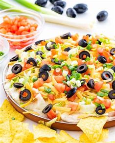 a pizza with black olives, tomatoes, cheese and tortilla chips on it