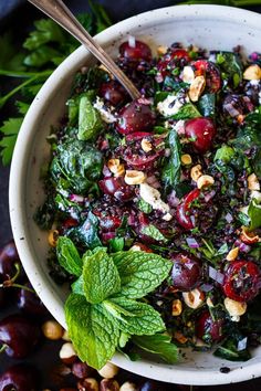 a salad with cherries, nuts and spinach in a white bowl on a table