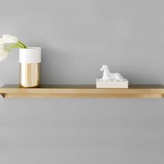 a vase with flowers and a white horse figurine on a shelf in front of a gray wall