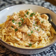 a white bowl filled with pasta covered in sauce and chicken meat on top of it