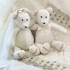 two white teddy bears sitting next to each other on top of a bed covered in lace