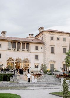 a bride and groom walk down the steps to their wedding ceremony in front of an elegant mansion