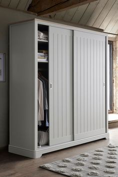 a large white closet with clothes hanging on it's doors and two baskets in front of it