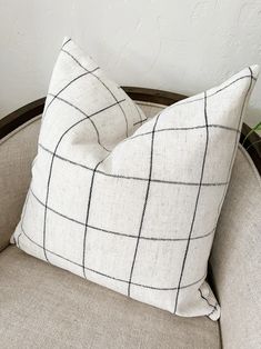 a white and black pillow sitting on top of a chair next to a potted plant