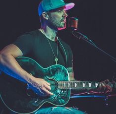 a man holding a guitar while sitting in front of a microphone and singing into a microphone