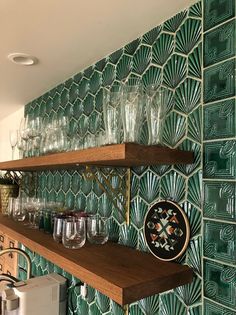 the shelves are filled with wine glasses and other items in front of a green tiled wall