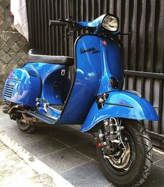 a blue motor scooter parked next to a fence