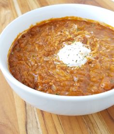 a white bowl filled with chili and sour cream on top of a wooden cutting board