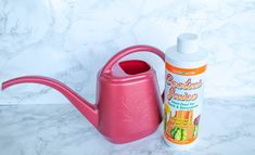 a pink watering can next to a bottle of insecticide