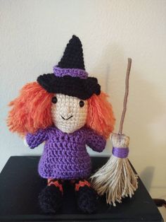 a crocheted witch doll sitting on top of a black table next to a broom