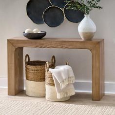 a wooden table topped with baskets next to a white vase and wall mounted art on the wall