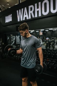 a man holding two dumbs in front of a gym