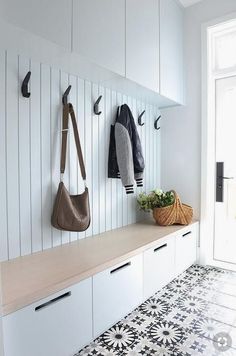 two coats hanging from hooks on the wall next to a bench with bags and purses