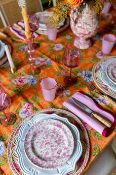 the table is set with pink and white plates, silverware, and orange napkins