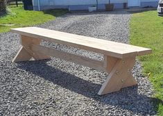 a wooden bench sitting on top of gravel next to a car parked in front of a house