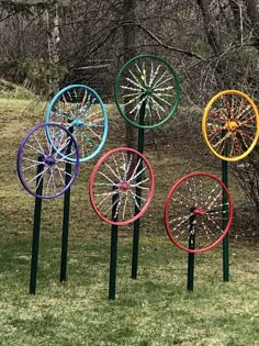 four colorful wheel sculptures in the grass near trees