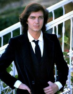 a man wearing a suit and tie standing in front of a stair railing with his hands on his hips