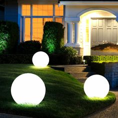 three glowing balls in front of a house at night with grass and bushes around it