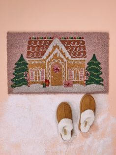 a pair of slippers sitting next to a door mat with a gingerbread house on it