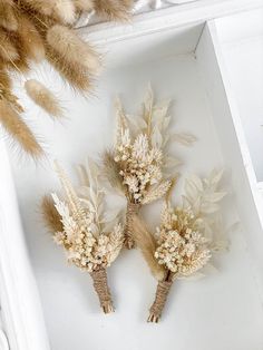 three dried flowers sitting on top of a white tray next to some dry grass and feathers