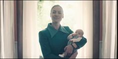 a woman holding a baby in her arms while wearing a green shirt and blue pants