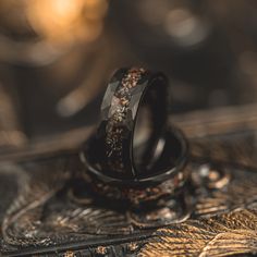 two wedding rings sitting on top of each other in front of a gold leaf pattern