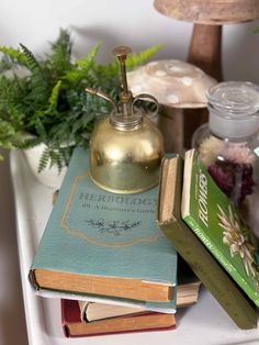 two books and a bell sitting on top of each other next to a potted plant