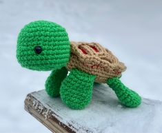 a small crocheted turtle sitting on top of a book in the snow,