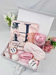 a pink gift box filled with personalized items and flowers on top of a white sheet