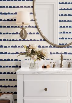 a bathroom with blue and white wallpaper and a round mirror on the wall above it