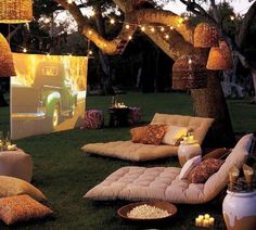 an outdoor movie is set up in the grass with lights strung from trees and hanging lanterns