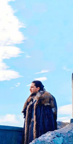 a man wearing a fur coat standing on top of a rock