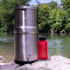 a red water bottle sitting on top of a rock next to a metal flask