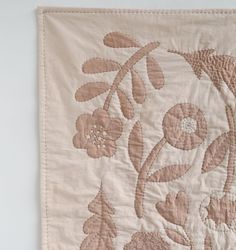 an embroidered wall hanging with pink flowers and leaves on it's side, in front of a white wall