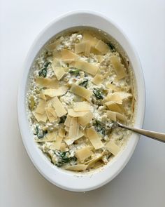 a bowl filled with cheese and spinach on top of a white countertop next to a spoon