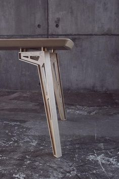 a wooden table sitting on top of a floor next to a cement wall with holes in it