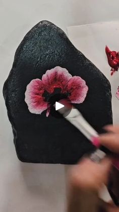 someone is painting a flower on a rock