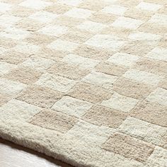 a close up of a rug on a wooden floor with white and beige squares in the middle