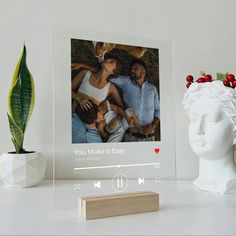 a white photo frame sitting on top of a table next to a potted plant