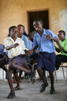 two young boys are dancing together in front of other children sitting at desks and chairs