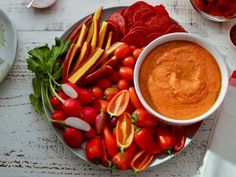 a plate full of vegetables and dip on top of a white table with utensils